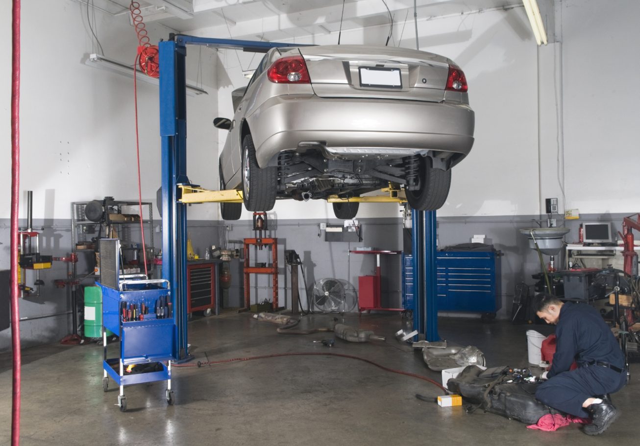 A car elevated on a lift in a workshop, with a technician working underneath. serviced near by me, garage car garage, garage near by me, 